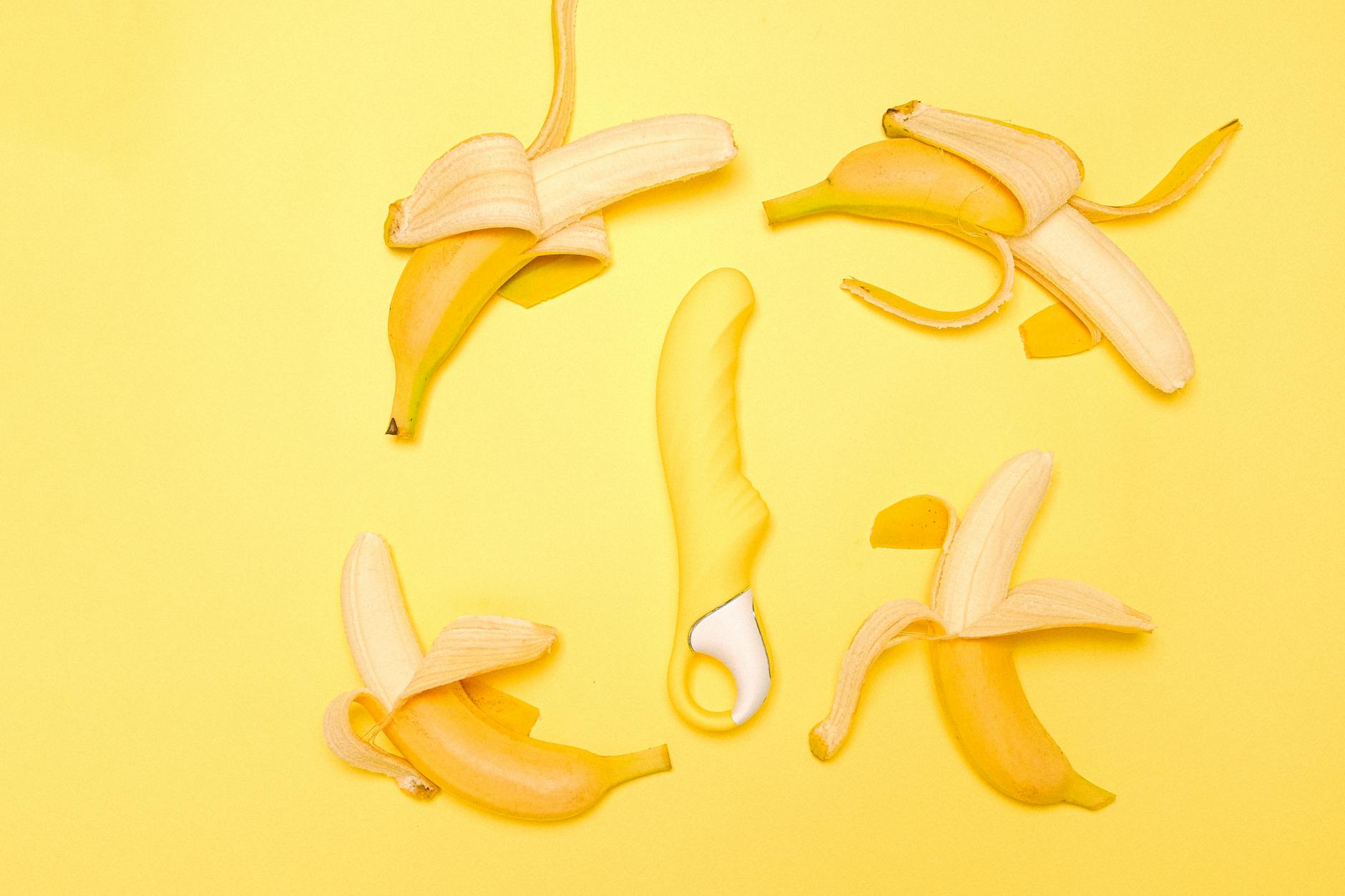 Yellow silicone lemon clitoral vibrator surrounded by fresh lemons and peeled banana segments on a bright yellow background