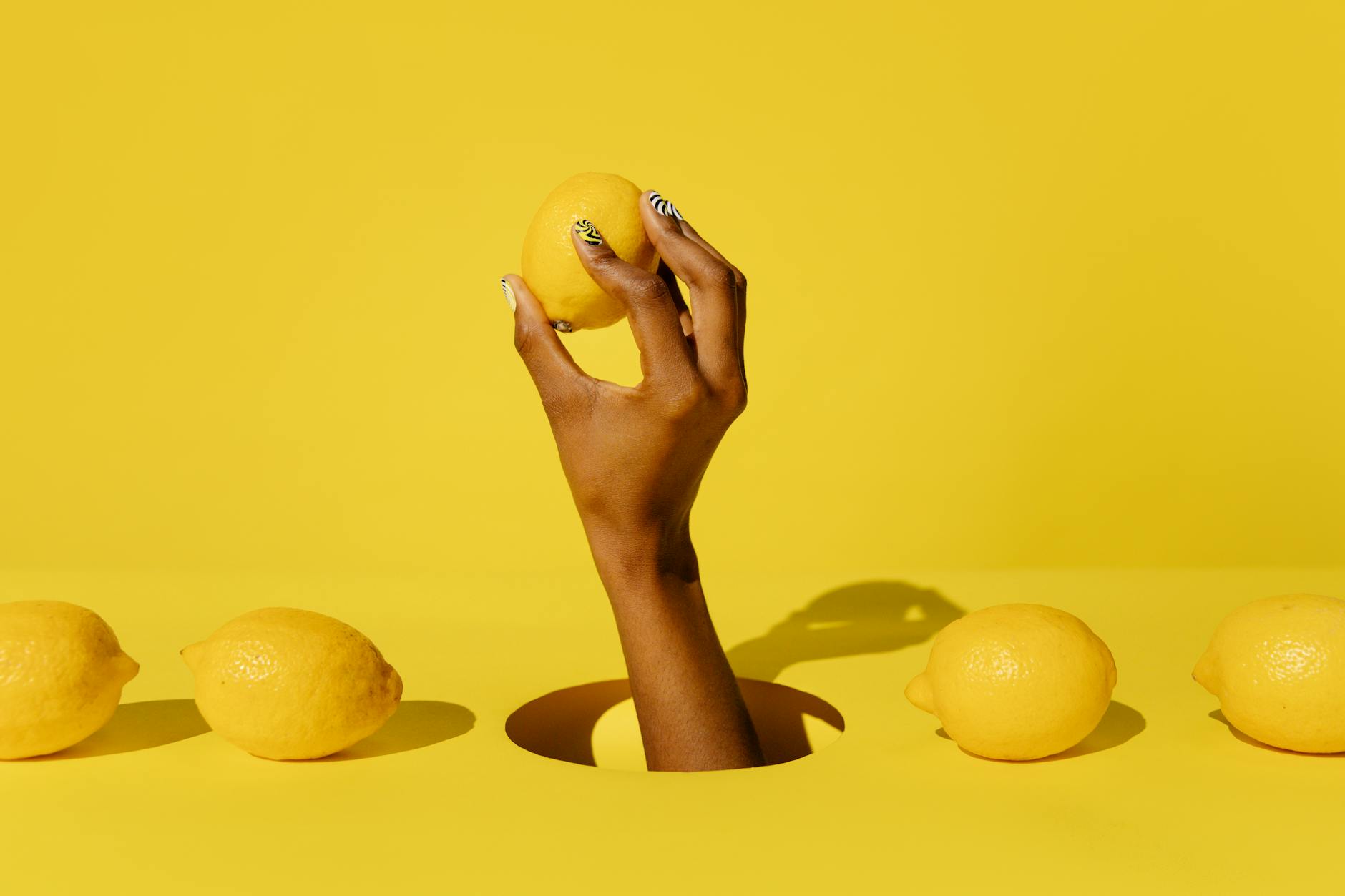 A creative composition featuring a hand holding a lemon against a vivid yellow background