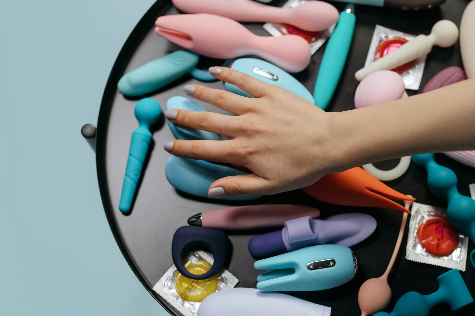 Deux mains tenant des vibromasseurs colorés sur une table avec une sélection de jouets