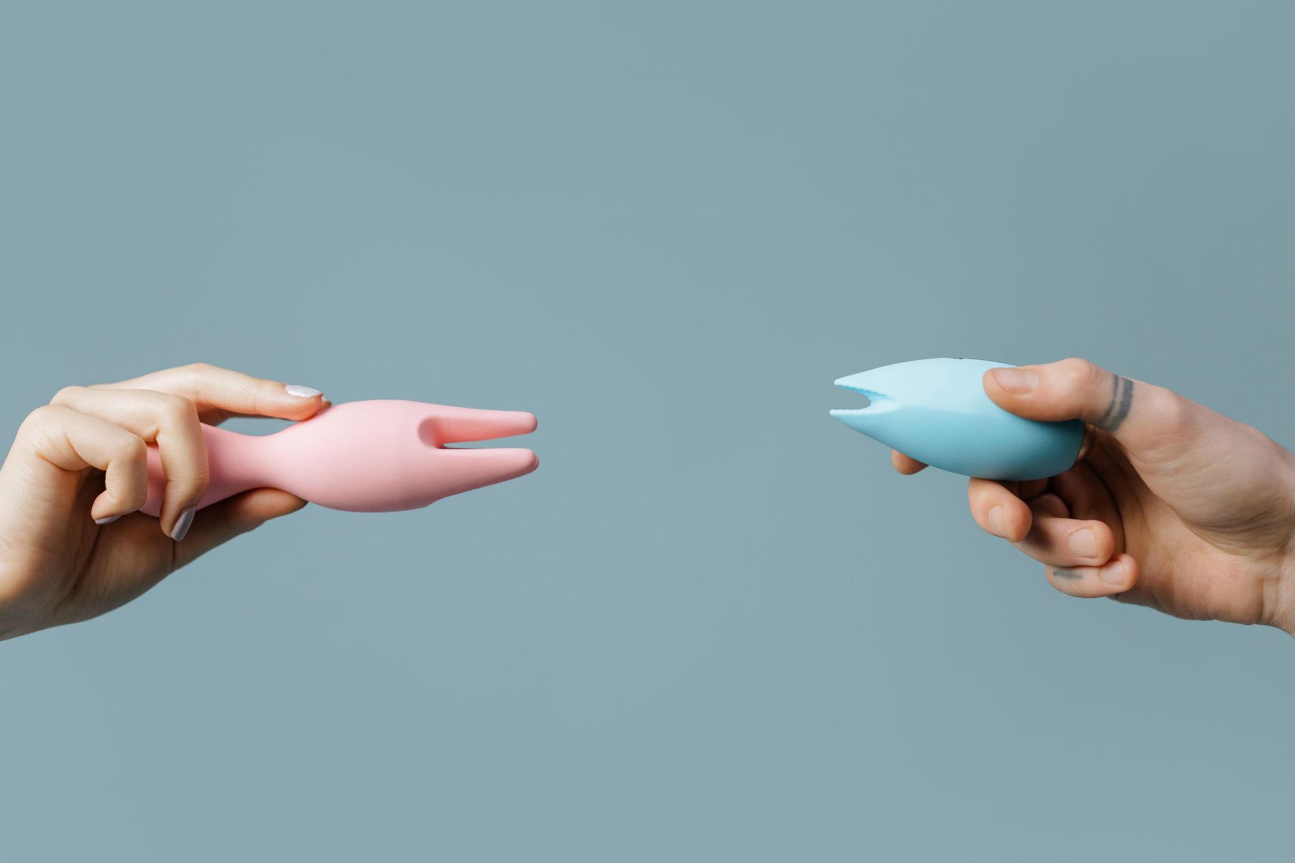 Two hands holding silicone vibrators against a pastel background, representing control and choice in pleasure.