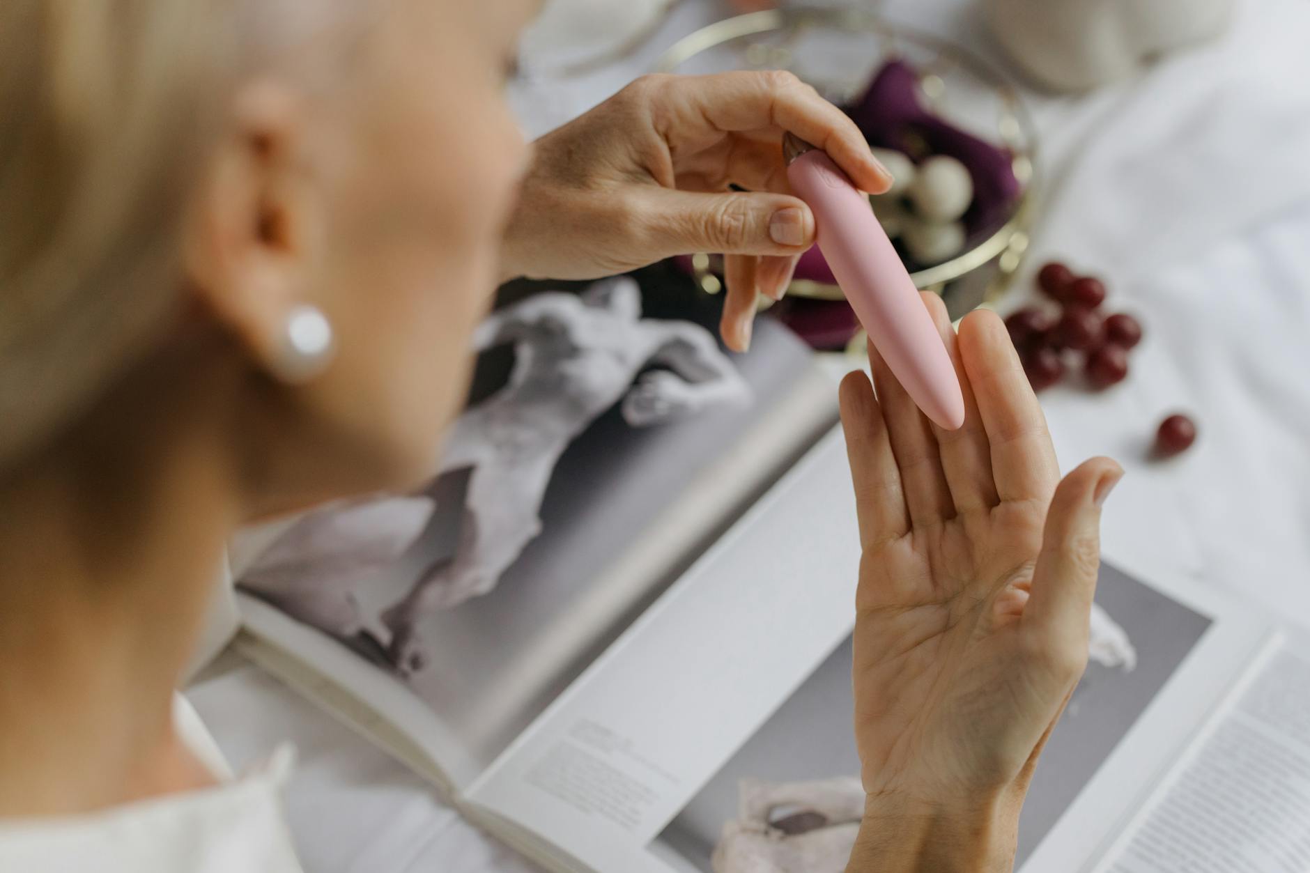 A person holding a pink vibrator with books nearby, symbolizing intimate personal moments and self-care.