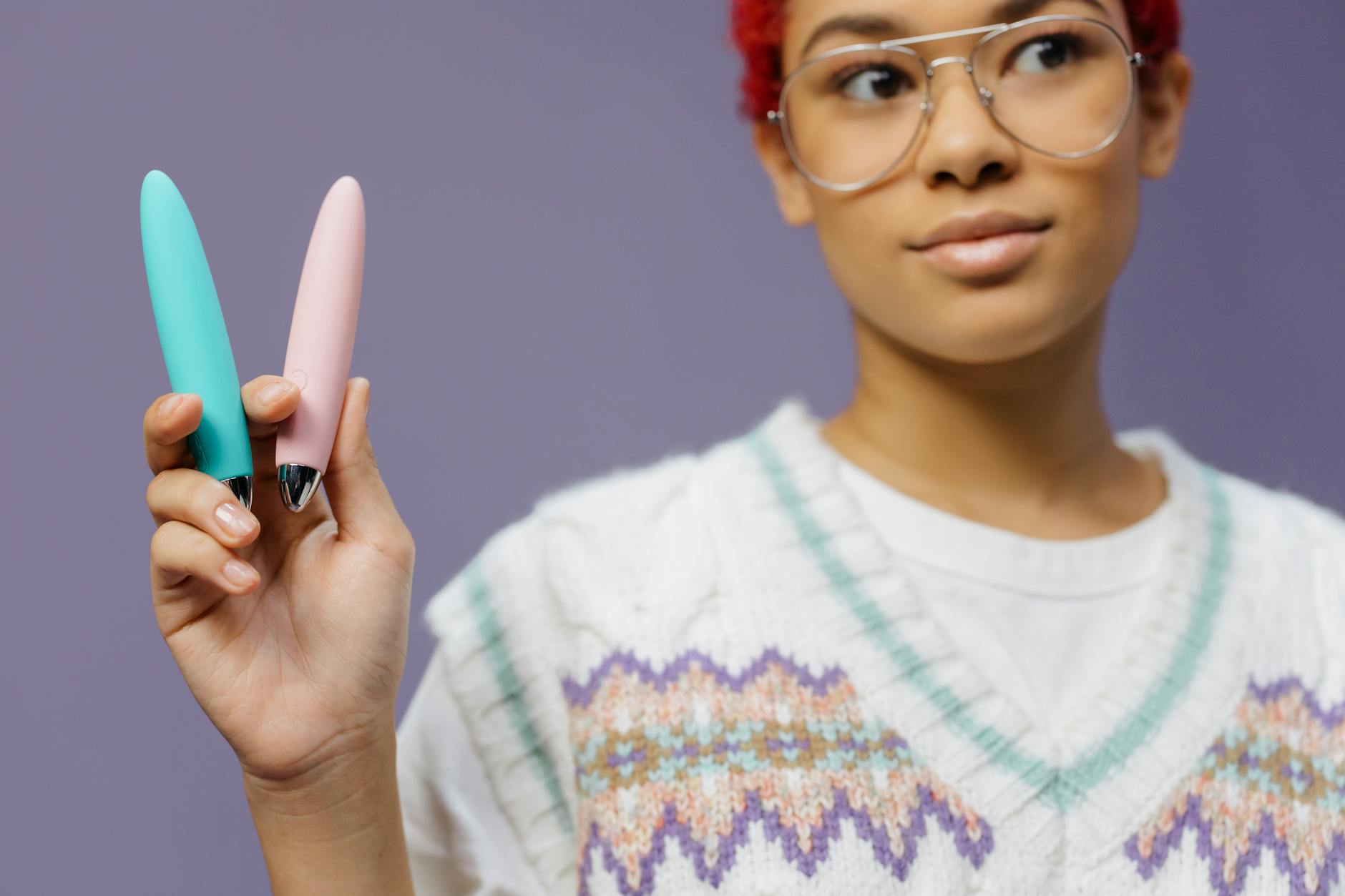 Une femme tenant deux vibromasseurs colorés contre un fond violet.