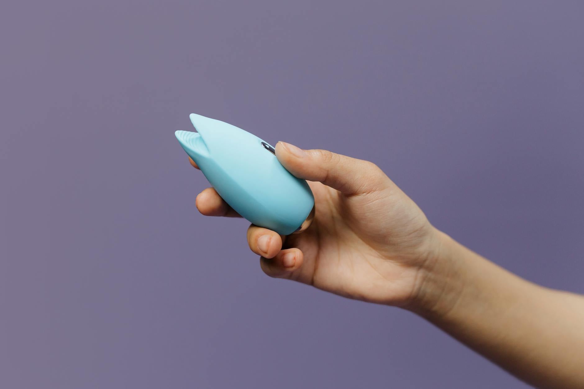 Un vibromasseur citron succion bleu tenu dans une main sur fond violet, promouvant l'auto-satisfaction et la sexualité