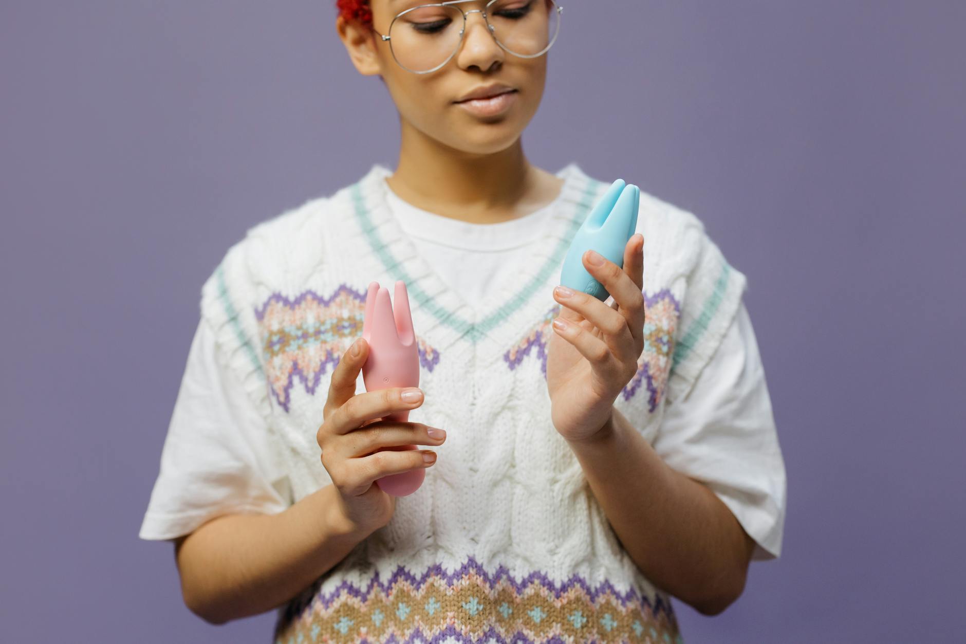 Woman holding blue and pink silicone vibrators in a contemplative manner, representing emotional connection to pleasure.