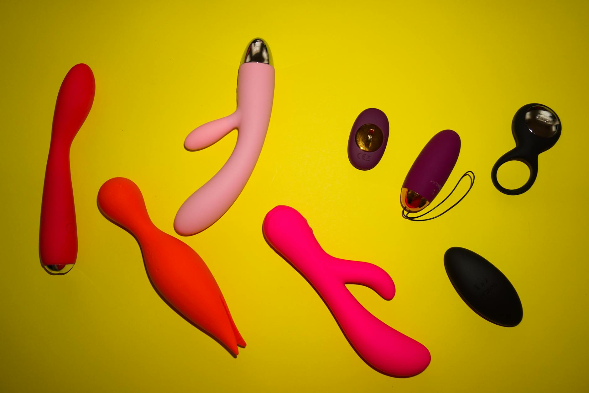 Vibrant collection of colorful clitoral vibrators and sex toys arranged on a bright yellow surface