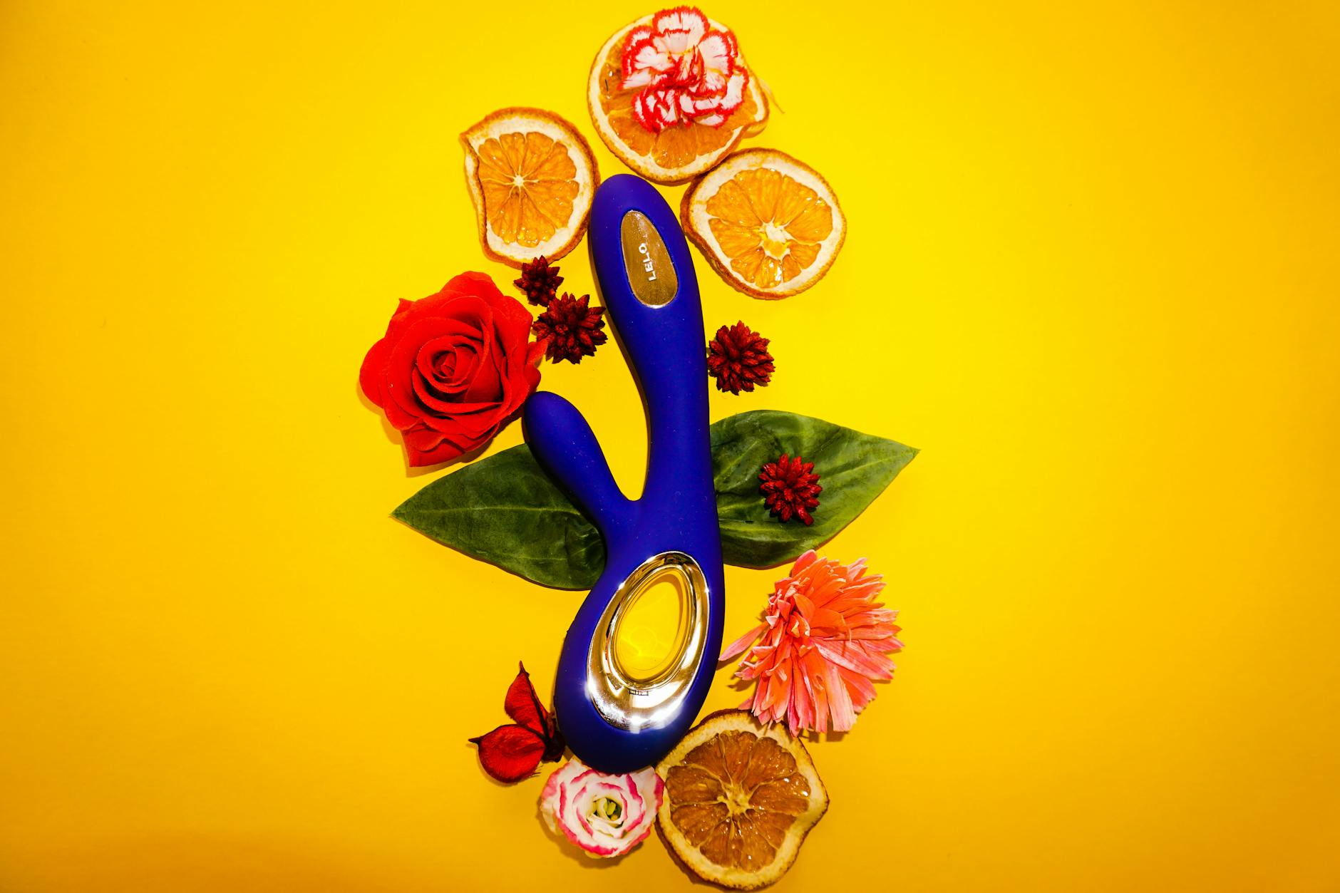 A blue lemon clitoral vibrator surrounded by flowers and citrus on a bright yellow background